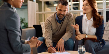 Happy couple having a meeting with financial advisor in the office. Man si signing a contract.