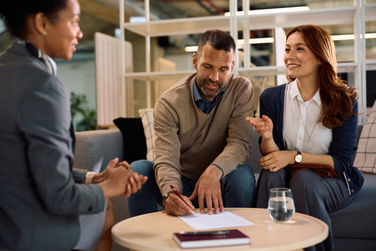 Happy couple having a meeting with financial advisor in the office. Man si signing a contract.
